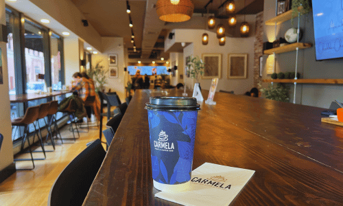 Greenwich Village Coffee Shops 21 Carmela Coffee Shop Greenwich Village cup of coffee on a wooden counter, with customers working and relaxing in the bright, modern café interior.
