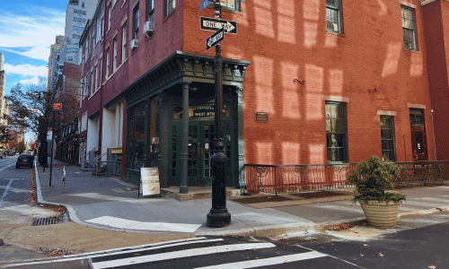 Stumptown Coffee Roasters in Greenwich Village – NYC Café 1 Corner view of Stumptown Coffee Greenwich Village showing the green-framed entrance, red-brick building, sidewalk sign, and quiet street intersection.