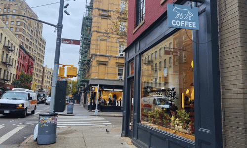 West Village Coffee Shops 27 Street view of Hungry Ghost Café in the West Village at Grove Street, showing the blue sign, large window, and warm interior with New Yorkers passing by.