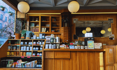 Stumptown Coffee Roasters in Greenwich Village – NYC Café 2 Inside Stumptown Coffee Greenwich Village showing wooden shelves, coffee beans, mugs, plants, and a classic wooden counter with warm lighting.