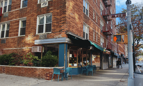 O Café Greenwich Village corner view with teal outdoor chairs, green awning, brick building, and a quiet street scene at West 12th Street.
