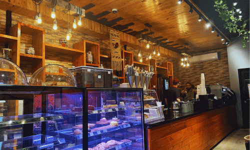 West Village Coffee Shops 25 Interior of Qahwah House in the West Village showing a warm wooden counter, pastry display, hanging lights, and baristas preparing authentic Yemeni coffee.