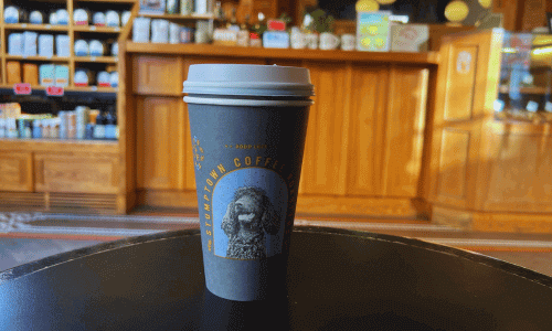 Stumptown Coffee Roasters in Greenwich Village – NYC Café 3 Stumptown Coffee Greenwich Village cup on a black table with the wooden café counter and shelves in the background.