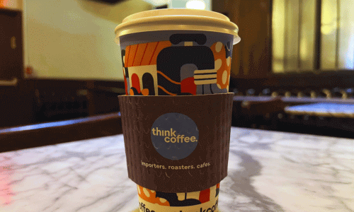 Think Coffee West Village – Fair-Trade Coffee Shop NYC 2 Close-up of a colorful Think Coffee cup on a marble table inside the West Village café, with warm lighting in the background.