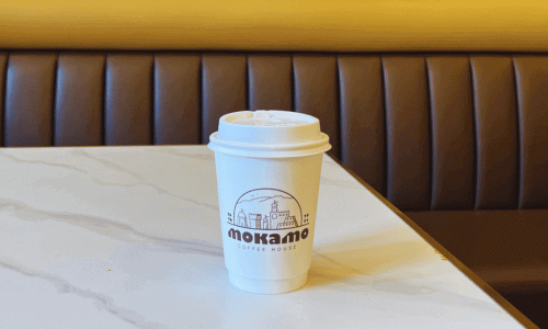 Moka Mo Coffee House Greenwich Village cup of coffee on a marble table with cushioned booth seating in the background.