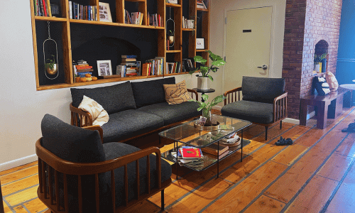 Moshava Greenwich Village features a cozy seating area with wooden floors, built-in bookshelves, modern sofas, and indoor plants.