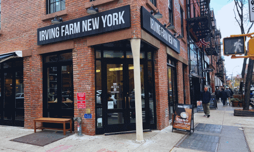 Irving Farm Greenwich Village exterior showing the brick corner building, black signage, large windows, and sidewalk sign near the front door.