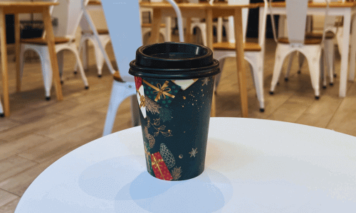 At The Venue Cafe Chelsea – Work-Friendly Coffee Shop NYC 3 A to-go coffee cup with a holiday-themed sleeve on a white table at The Venue Cafe in Chelsea.