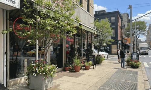 Café Flor Chelsea exterior with sidewalk seating, large windows, street greenery, and pedestrians in the Chelsea neighborhood of Manhattan.