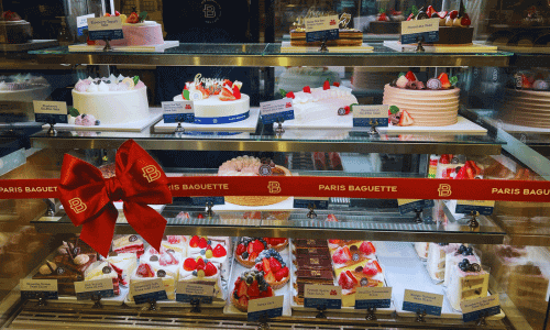 Cake display at Paris Baguette in Chelsea, Manhattan, featuring assorted decorated cakes and pastries behind a glass case.