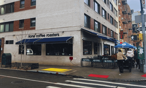 Exterior corner view of Kona Coffee Roasters Chelsea with outdoor seating and blue awning.