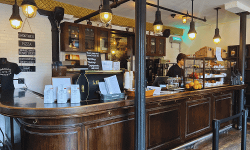 The espresso bar at Kobrick Coffee West Village featuring a vintage wooden counter, hanging pendant lights, coffee equipment, and the classic café setup.