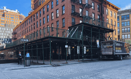 Street corner view outside Kobrick Coffee West Village showing the historic brick building, sidewalk scaffolding, and surrounding West Village streetscape.