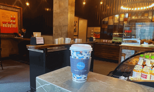 Interior of Think Coffee near Hudson Yards in Chelsea featuring a coffee cup on the counter, pastry display case, and warm wood and tile décor.