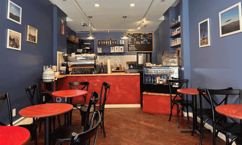 Absolute Coffee West Village – Best Coffee in NYC 1 Inside Absolute Coffee West Village featuring red tables, black chairs, espresso bar, and pastry display counter.