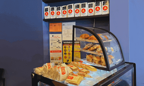 Absolute Coffee West Village – Best Coffee in NYC 2 Glass display case with pastries and packaged snacks beneath shelves of coffee bags at Absolute Coffee West Village.